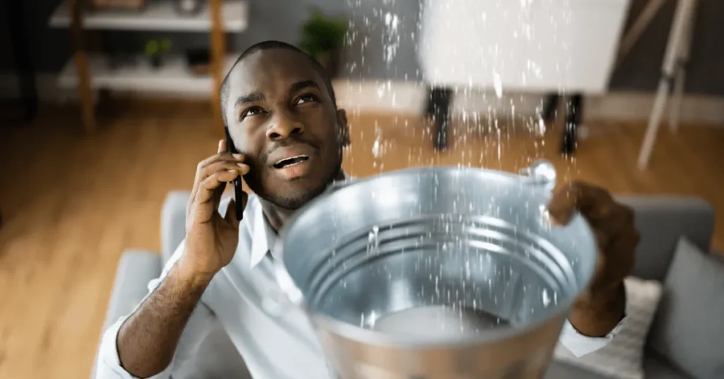 Homeowner catching leaking water in a bucket while calling an emergency plumber in Whitstable